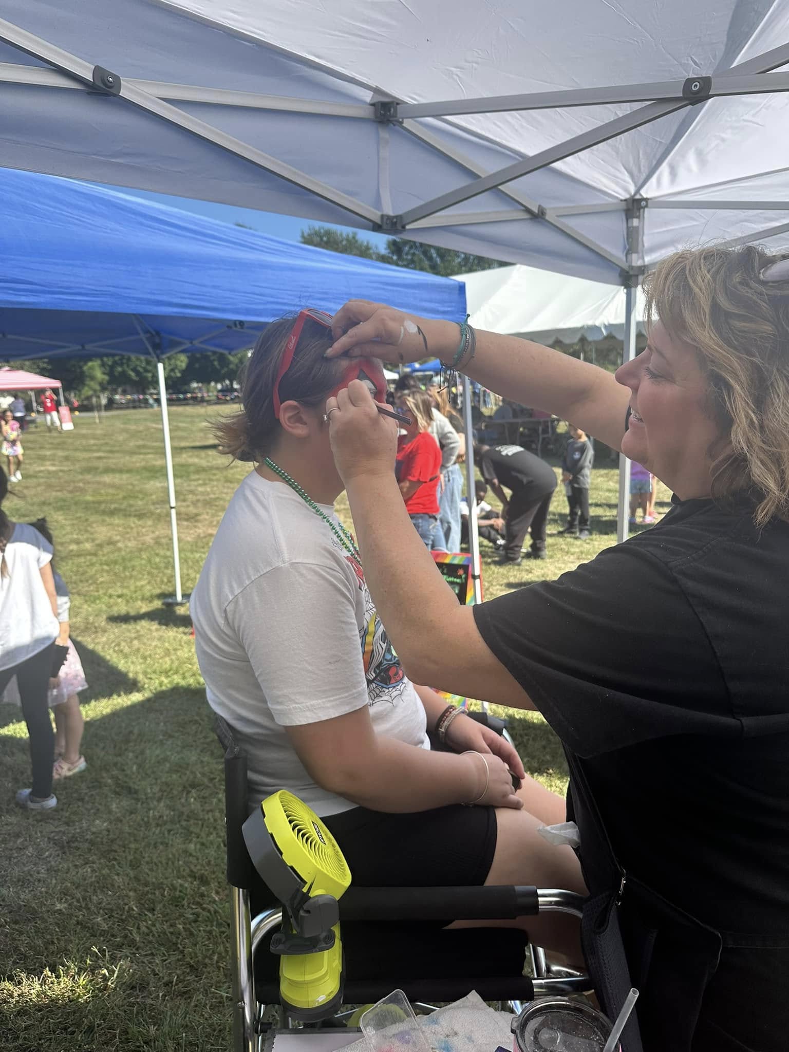 A face painter working under a canopy while a child waits