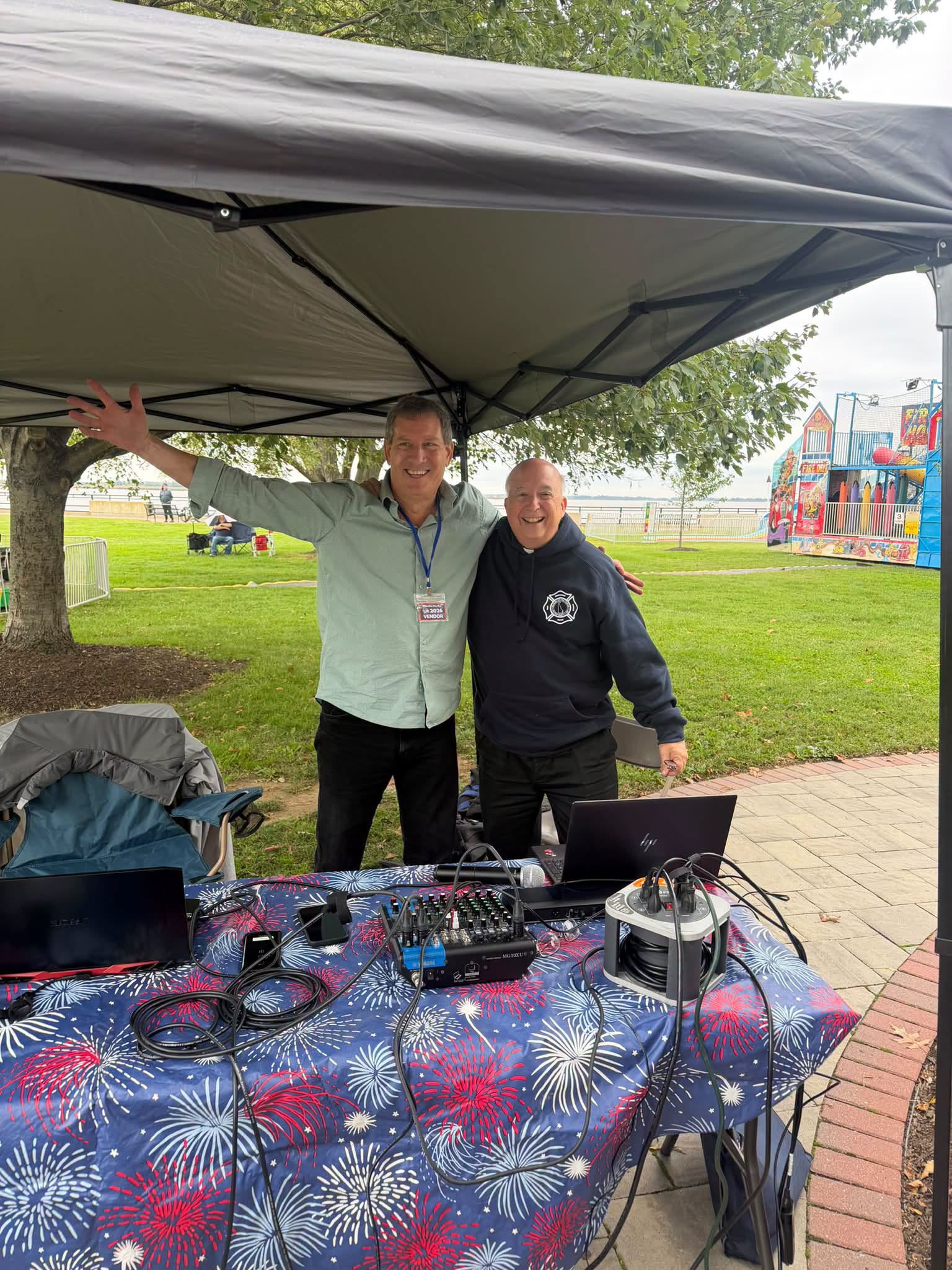 Two men working beside DJ and audio equipment under a white canopy