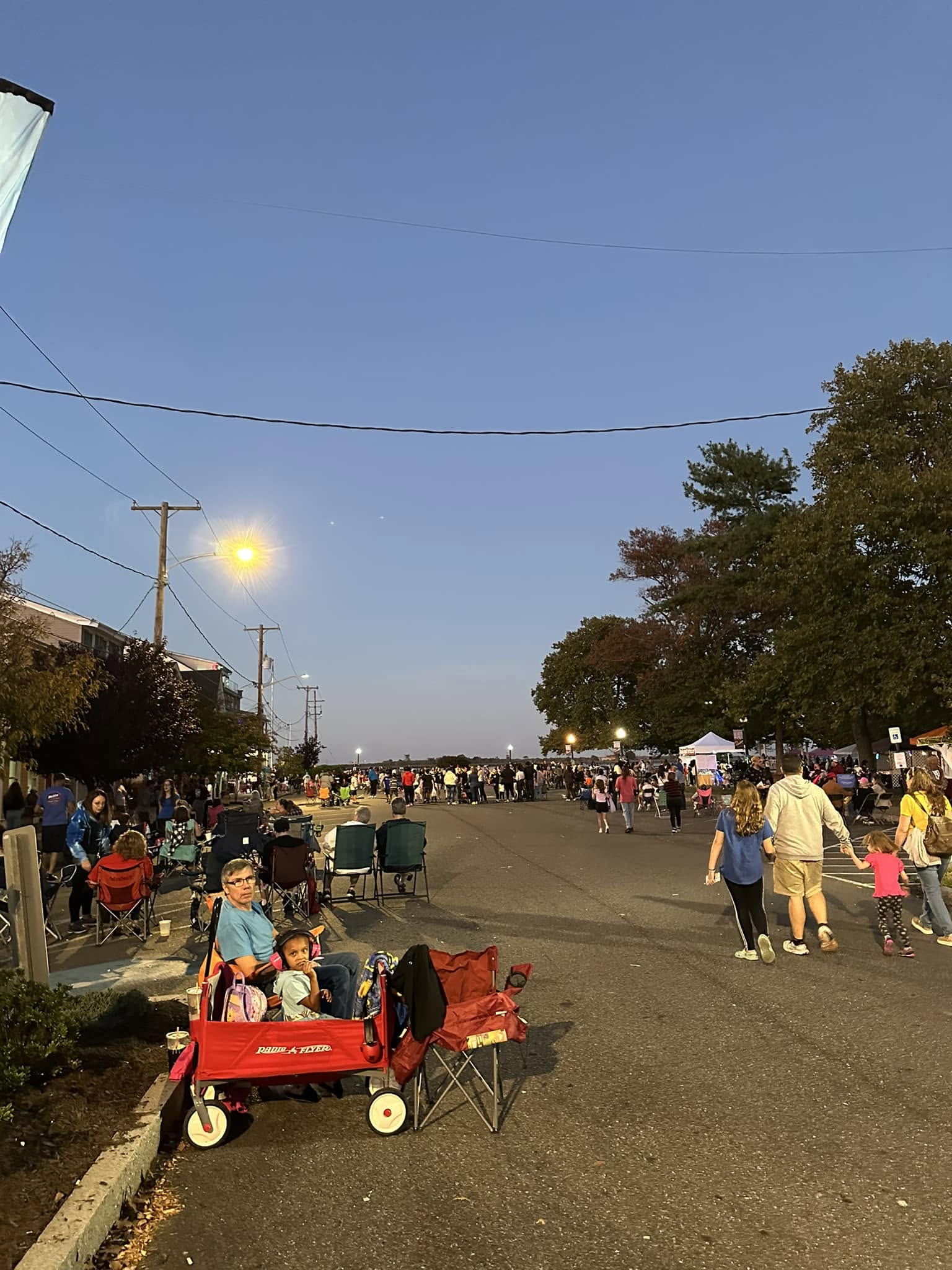Attendees walking across the field at dusk, two toddlers riding in a red wagon