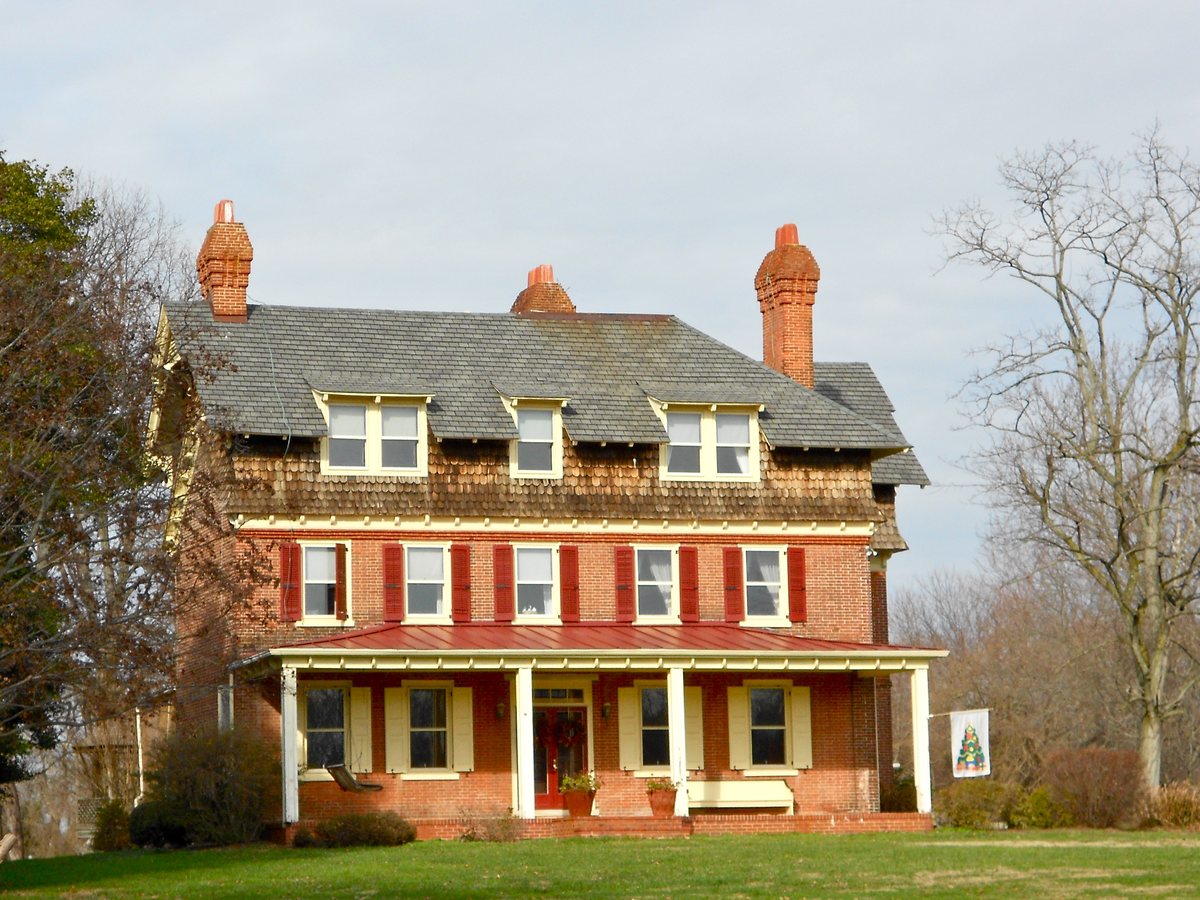 Large Victorian house with a shingled upper story, brick chimneys and a columned veranda