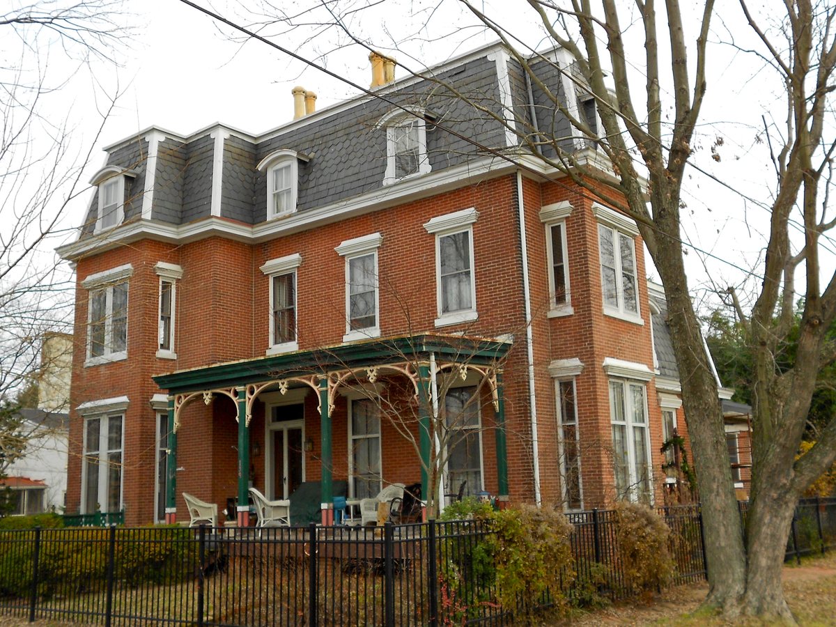 Red brick Second Empire home with a mansard roof and decorative porch