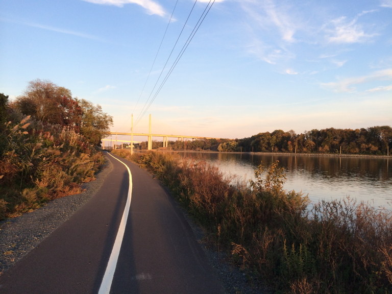 Michael N. Castle Trail beside the canal in warm evening light, with autumn trees and a distant bridge