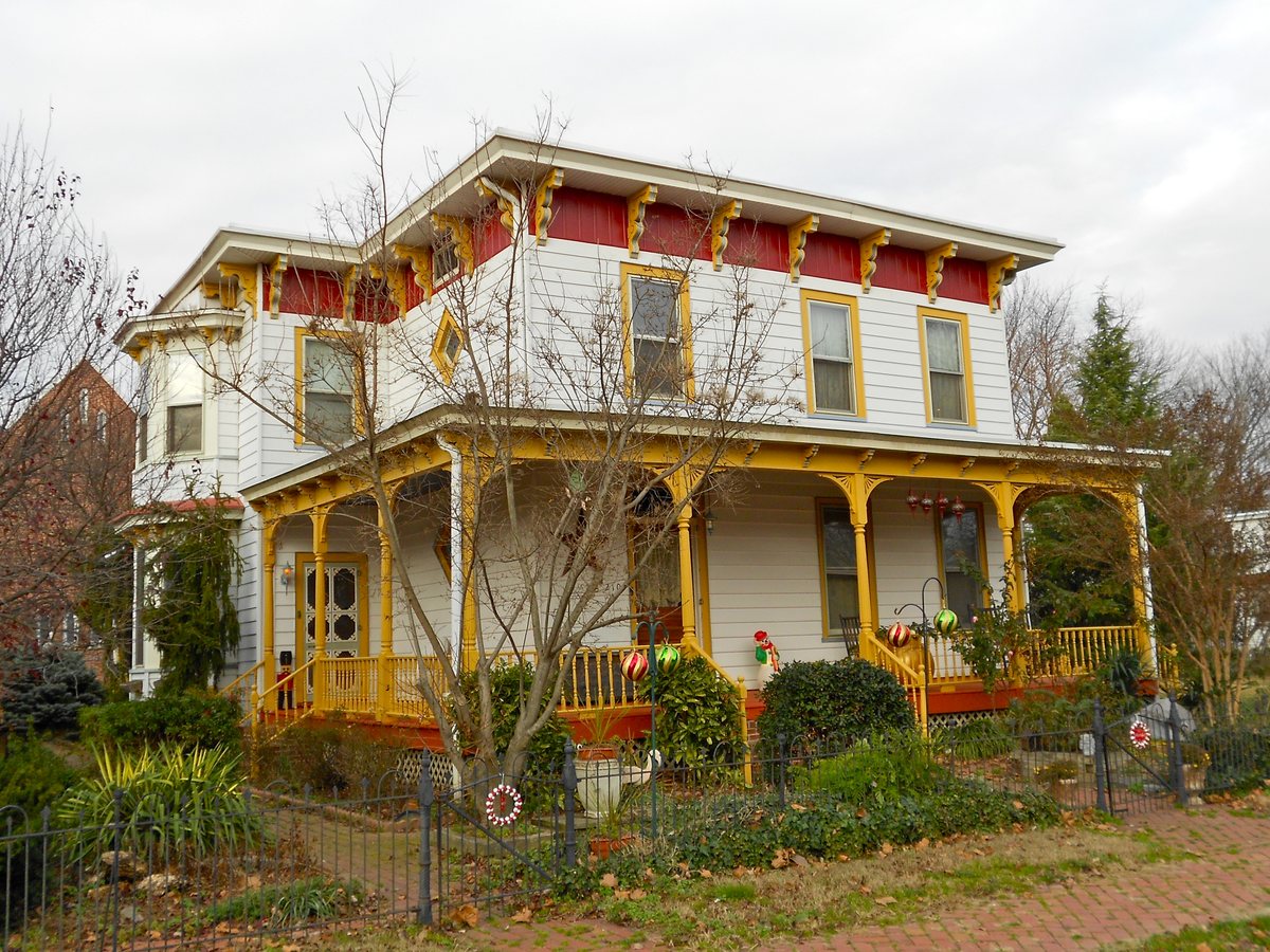 White clapboard home with a wraparound porch and yellow and red trim