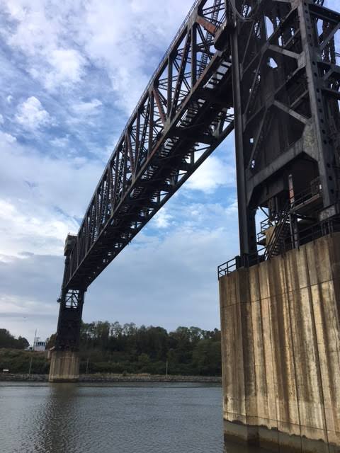 View beneath a tall steel truss bridge spanning the canal, with concrete piers beside the water